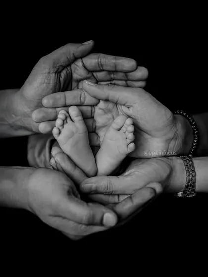 A timeless black and white photograph showing a newborn's tiny feet held securely in the hands of their family. We focus on these small, precious details that tell a big story of love and connection.