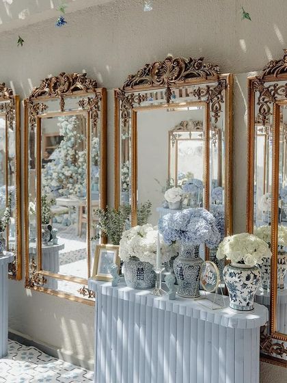 A row of ornate, gold-framed mirrors reflects the beautiful blue and white decor of the baby shower.