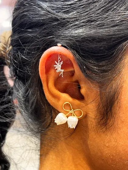 A whimsical ear curation with a delicate fairy hanging from the helix, paired with unique floral and bow earrings on the lobe.