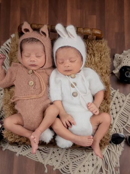 Newborn twins dressed in adorable bunny-ear outfits sit together, posed with retro props like sunglasses and a vintage radio.
