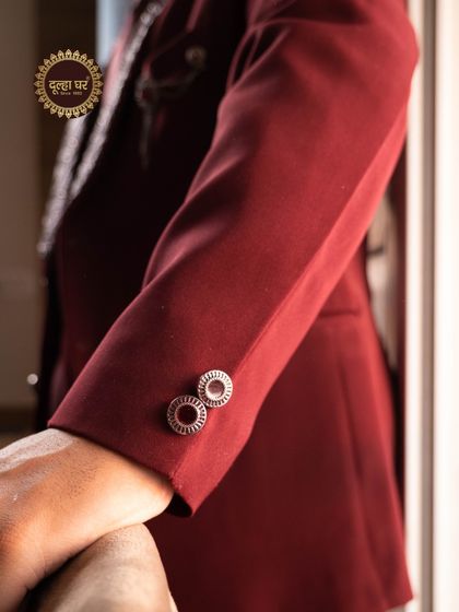 Details that define elegance. A close-up on the sleeve of a maroon suit, showing the custom, jewel-like buttons.