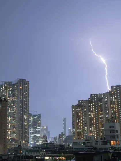 A powerful lightning bolt illuminates the clouds as it strikes down behind a building in Mumbai.
