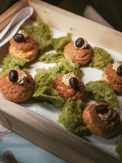 Elegant coffee-filled choux pastries presented on a bed of pistachio moss. These delicate, airy buns are a sophisticated pick-me-up, combining classic French pastry with rich coffee flavor.