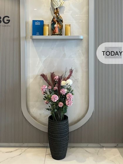 A designer cement planter with a textured black finish, filled with beautiful artificial flowers. This makes a stunning statement piece for an entryway.