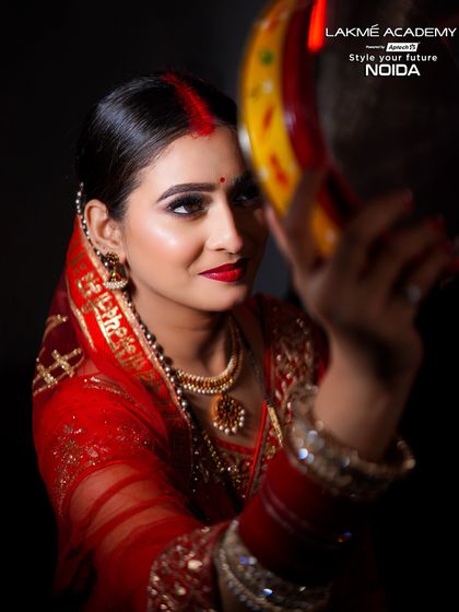 A beautiful Karwa Chauth look, featuring a woman in a traditional red saree looking at the moon through a sieve. We teach festive makeup for all important cultural occasions.