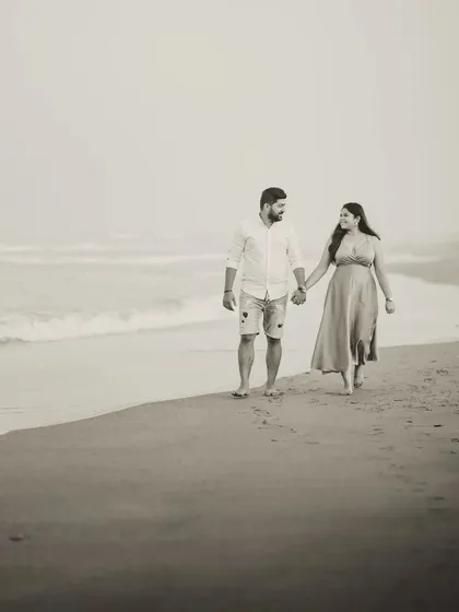 A classic walking shot of Milando and Joann on the beach, rendered in a soft, sepia-toned black and white for a nostalgic, film-like quality.