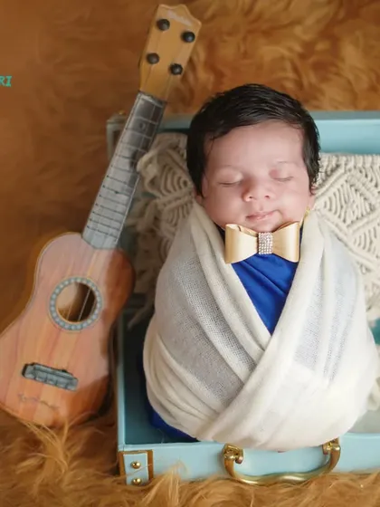 A little musician in the making. This newborn is posed in a vintage-style suitcase with a tiny guitar, showcasing a creative and personalized setup.