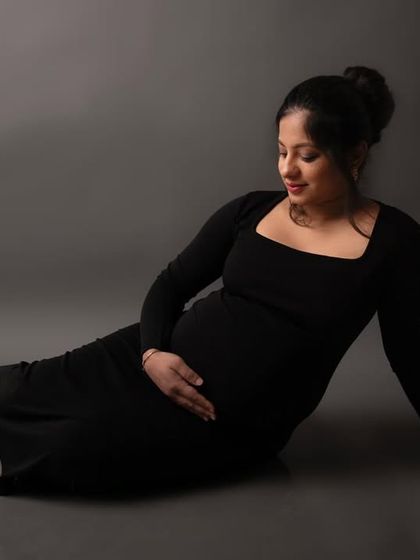 A simple, classic pose in a black gown against a grey backdrop. This timeless portrait beautifully highlights the curve of the baby bump with soft, elegant lighting.
