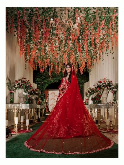A stunning portrait of the bride under a canopy of hanging flowers. The long red veil of her lehenga creates a dramatic and beautiful effect.