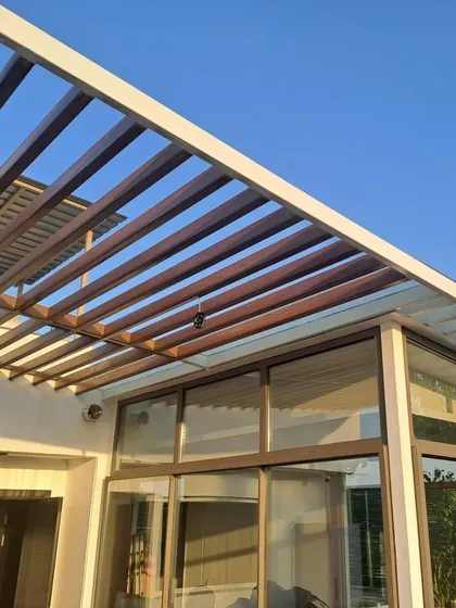 A look at a completed rooftop sunroom, featuring a modern wood-slat pergola over a glass and steel frame. This project transformed an open terrace into a usable, all-weather living area that feels both spacious and connected to the sky.