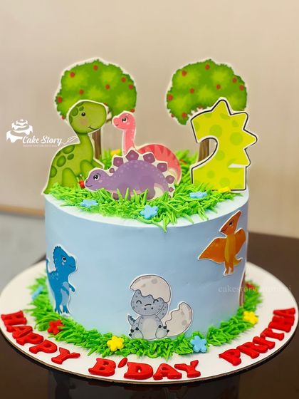 A cute dinosaur cake for a second birthday. This blue cake is decorated with green grass piping and adorable cartoon dinosaur toppers.