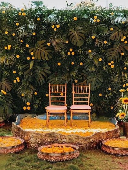 A tropical-themed Haldi backdrop featuring a wall of monstera leaves dotted with yellow marigolds. This is a great way to add a modern, green twist to the ceremony.