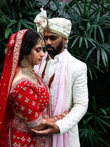 An intimate embrace against a backdrop of dark green leaves. The contrast makes the couple's red and white outfits pop.