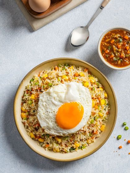 A top-down view of a bowl of mixed vegetable and egg fried rice, topped with a fried egg.