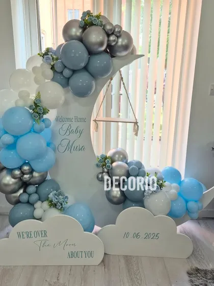 For a dreamy welcome home party, I created this "Over the Moon" setup. It features a custom-built moon prop with a tiny swing, surrounded by a cloud of blue, white, and silver balloons, making it a perfect welcome for a baby boy.