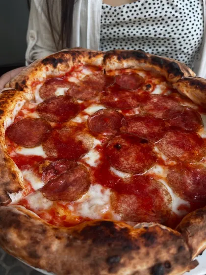 Someone holding our Hungarian Salami pizza. It's a pie that's meant to be shown off before it's devoured.