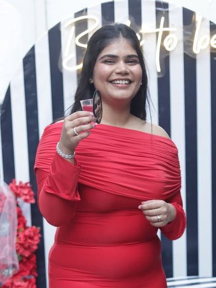 The bride-to-be, radiant in red, raising a toast to her upcoming wedding.