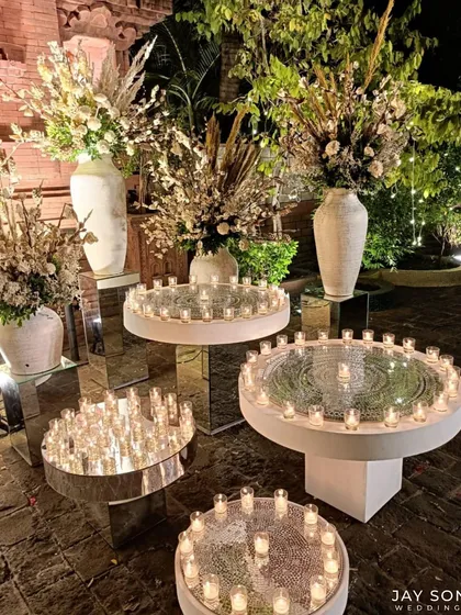 An installation of candles on mirrored tables, creating an infinite reflection of warm light, complemented by large vases of pampas grass and dried florals.