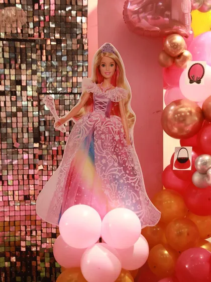 A beautiful Barbie cutout in a rainbow gown stands tall on a balloon pillar, adding a touch of sparkle and magic to the party decor.