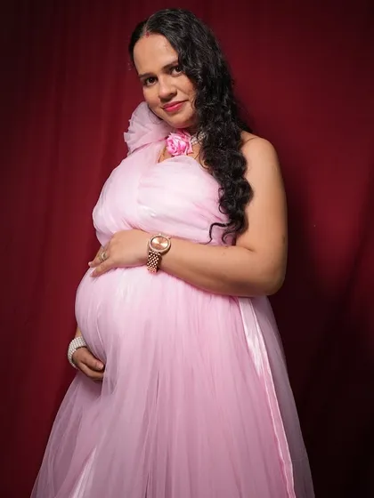 A beautiful close up portrait from a maternity session. The client is wearing a flowing pink tulle gown, and the studio lighting perfectly highlights the happy expression and the baby bump.
