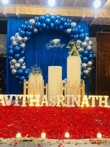 A blue and silver balloon arch with a dramatic red rose petal floor and candles.
