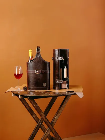 A still life of Verman Atelier's leather wine carriers on a rustic wooden table. This image creates an atmosphere of refined taste, perfect for a wine connoisseur.