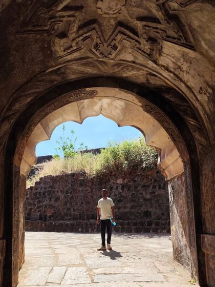 A trekker framed by an ancient stone archway, likely at a historical site visited during the Kumara Parvatha trek.