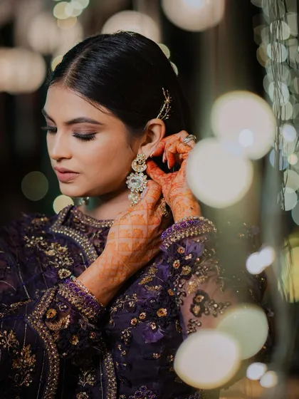 A detailed shot of the bride adjusting her earring, with beautiful bokeh lights in the background.