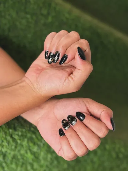 Another view of the black and foil manicure, showing how the light reflects off the metallic accents against the deep black base.