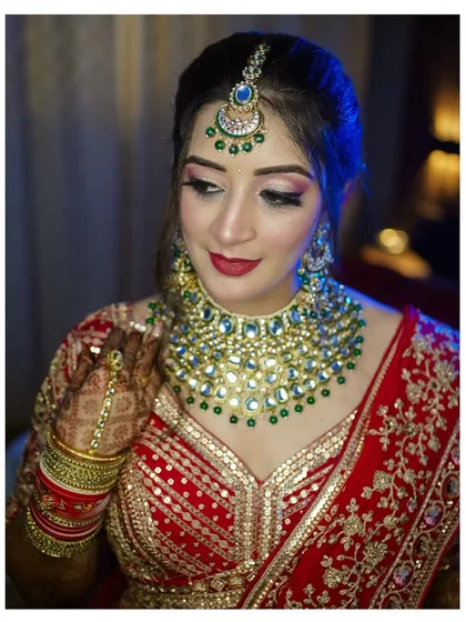 A stunning portrait of a Punjabi bride looking down at her henna-covered hands. The blue backlighting adds a touch of modern drama to her traditional red lehenga and green kundan jewelry.