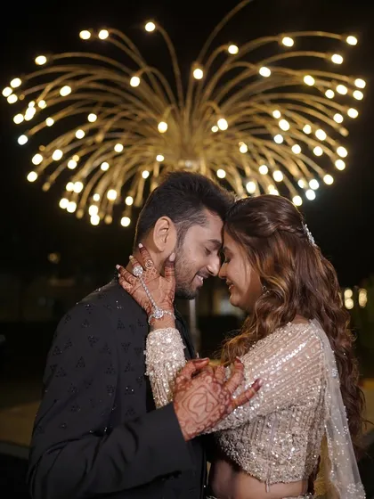 A romantic close-up of the couple. The bride's sangeet look features soft curls, a delicate haathphool, and shimmery makeup that catches the light perfectly.