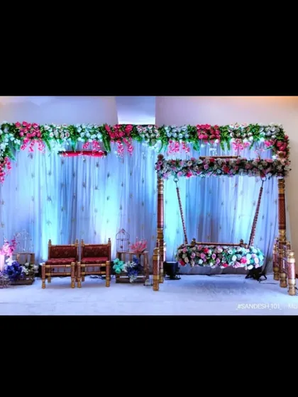 A beautiful stage for a naming ceremony. The decor includes an elegant floral jhula, seating for guests, and a white curtain backdrop with floral arrangements.