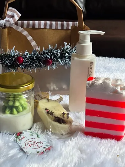 This Christmas gift set includes a striped soap, a tree-in-a-jar soy candle, a wax sachet for wardrobes, and body lotion, all presented in a festive basket.