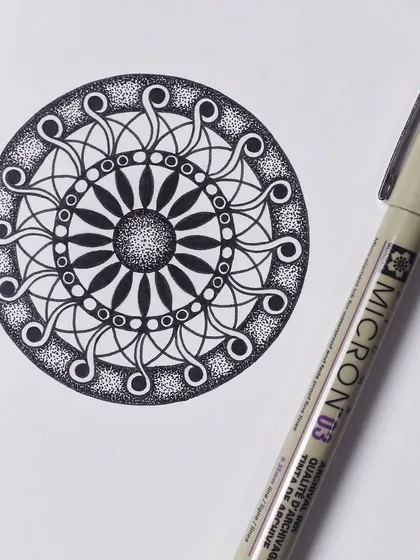 A circular mandala design created with a Micron 03 pen. The pattern uses repeating swirls and stippling to create a sense of movement and depth.