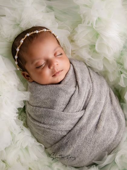 A beautiful portrait of a baby girl in a simple grey wrap, nestled in a bed of soft, light green tulle for a dreamy effect.