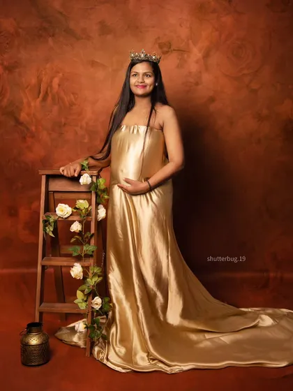 A classic pose with our golden satin gown against a warm, textured backdrop. The addition of a small ladder prop with flowers adds a touch of rustic charm to this glamorous shot.