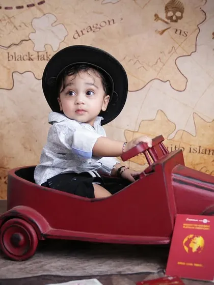 A baby boy ready for an adventure in his travel-themed photoshoot, complete with a hat, toy car, and passport.