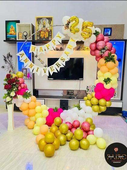 A vibrant and colorful ring setup for a 25th anniversary at home. This decoration uses a mix of pastel and gold balloons, a floral arrangement, and a "Happy Anniversary" banner.