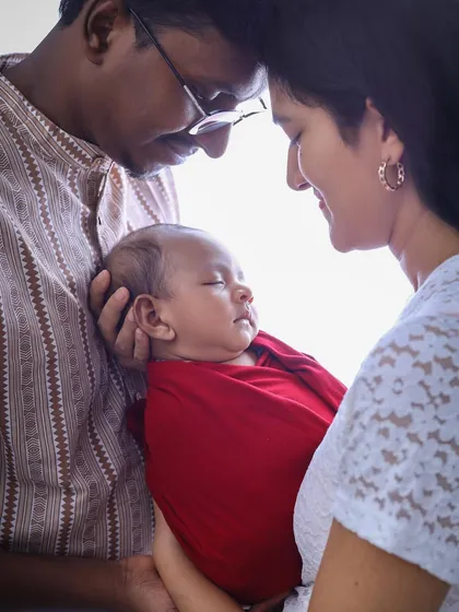 A tender moment between parents and their sleeping newborn. The soft, bright light creates a halo effect, emphasizing the peaceful and loving atmosphere of this family portrait.