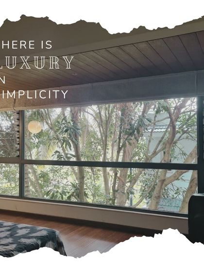 "There is luxury in simplicity." This image of a bedroom with a large window overlooking lush trees perfectly captures our belief that true luxury comes from a connection with nature and uncluttered living.