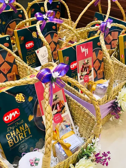 Another angle of the beautifully assembled wedding return gift baskets. The purple ribbon and floral accents on the wicker baskets create a cohesive and elegant look for thanking guests at a special event.