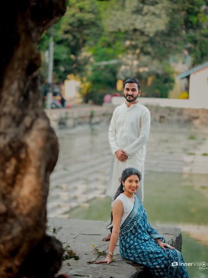 A beautifully framed shot of the couple near a temple pond. The tree in the foreground adds depth, creating an artistic and serene portrait.