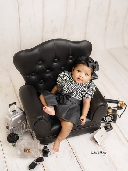 A classic "Boss Lady" pose. This baby is sitting comfortably in her mini leather armchair, looking every bit the part of a tiny CEO.