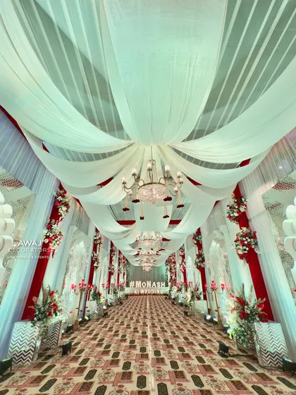 A truly grand and regal walkway, with a ceiling of billowing white drapes, crystal chandeliers, and red and white floral accents.