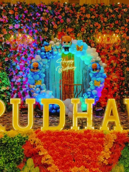 This is an example of a dense, high-impact backdrop. I built a complete wall of colorful artificial flowers and layered it with a blue balloon circle, a 'Happy Birthday' neon sign, and large, bright marquee letters for the name 'RUDHAV'.