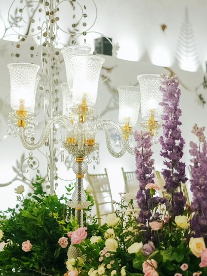 An elegant glass candelabra surrounded by lush purple and pink flowers. This was part of the decor for the grand reception entrance, adding a touch of classic luxury and vibrant color.