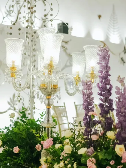 An elegant glass candelabra surrounded by lush purple and pink flowers. This was part of the decor for the grand reception entrance, adding a touch of classic luxury and vibrant color.