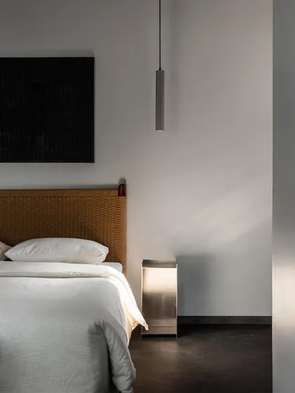 The sunlit master bedroom, highlighting the texture of the handwoven headboard. The play of light and shadow across the materials is a key part of creating a dynamic yet peaceful space.