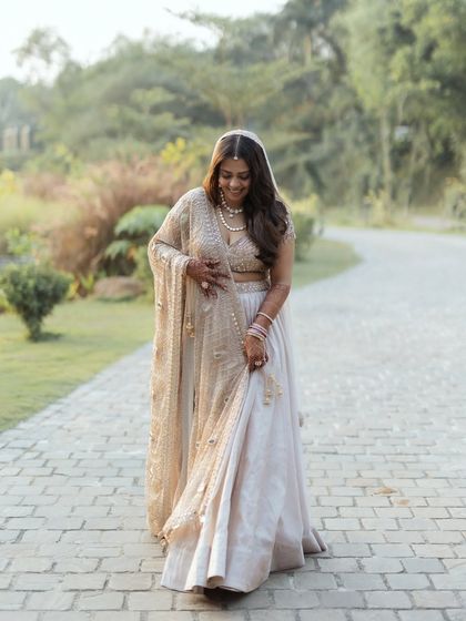 A beautiful, candid portrait of a bride in a soft, elegant lehenga. Her gentle smile as she walks through a garden path gives this shot a natural and dreamy feel.
