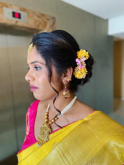 A classic South Indian bridal updo, adorned with a mix of yellow and pink flowers to match the bride's beautiful Kanjeevaram saree.